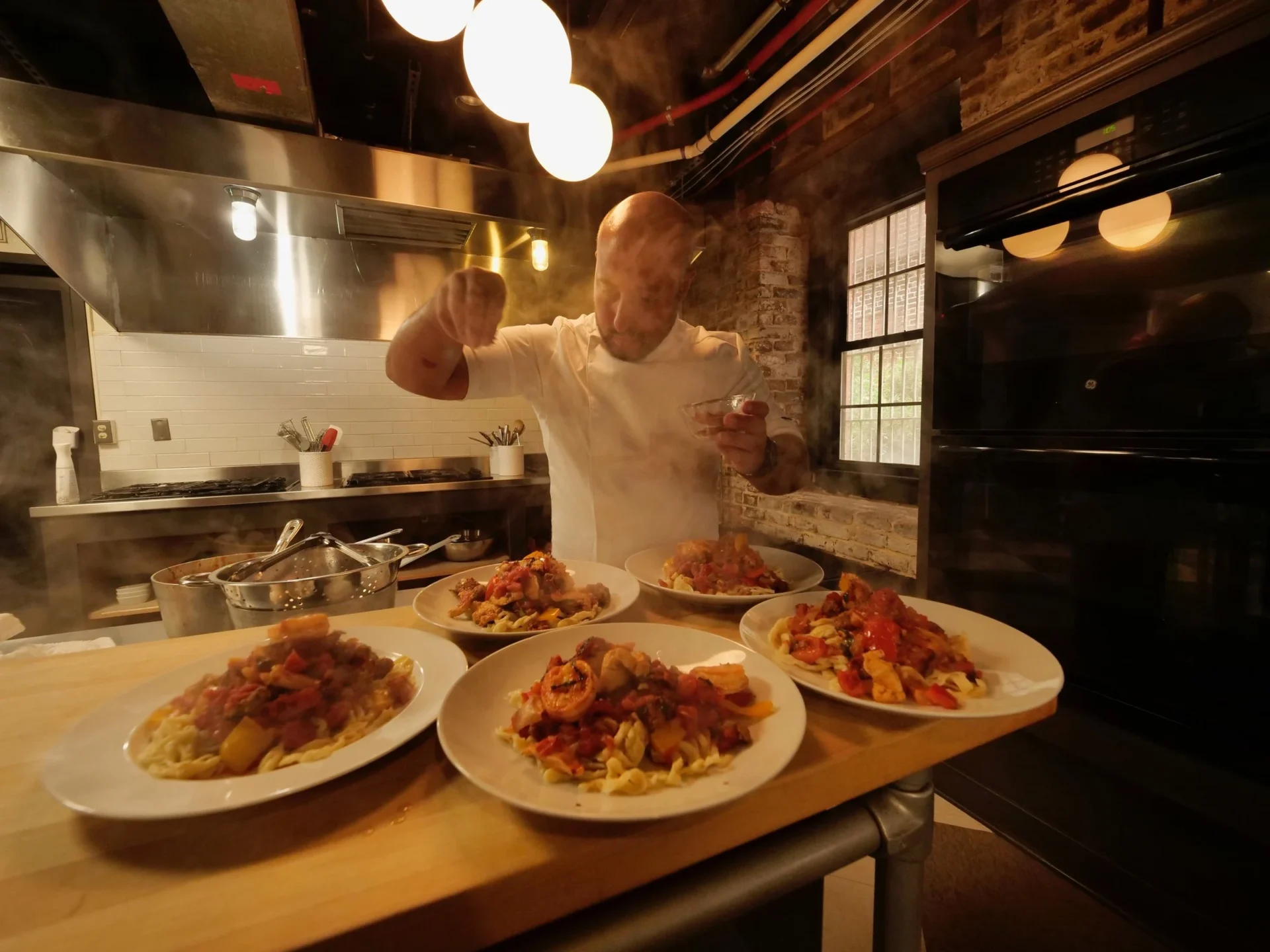 Chef seasoning plates of pasta in kitchen.